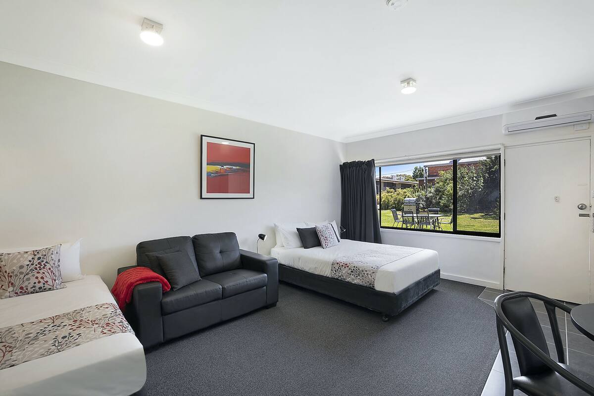 Quarto de hotel com cama, sofá, mesa de jantar e janela com vista.