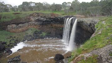 A waterfall cascading into a rocky pool surrounded by grassy terrain and trees.