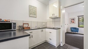 A modern kitchen with white cabinets, a microwave, and a sink. There is a framed artwork on the wall and a blue chair in the corner. - Hamilton Lakeside Motel (Hamilton)