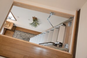Un espejo con marco de madera que refleja una escalera, una planta colgante y un radiador.