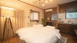 A bedroom with a bed, a standing lamp, a clock, a brick wall, and a kitchen area. - Kanegafuchi House (Tokyo)
