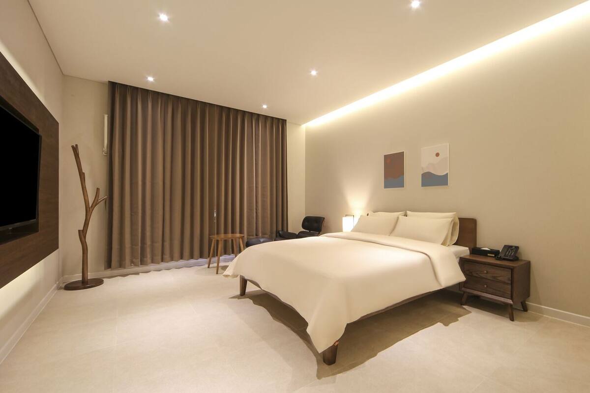 A modern hotel room with a large bed, bedside tables, a TV, and a window with curtains.