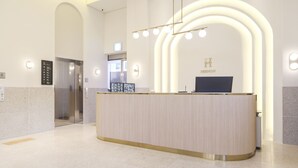 A modern reception desk with a curved design, a glass elevator, and a sign reading "HERMON". - Hermon Hotel Gangseo (Busan)