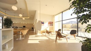 A modern interior with a kitchen, dining area, and seating space with large windows. - Hermon Hotel Gangseo (Busan)