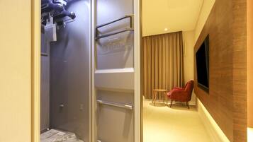 A hotel room with a walk-in closet, a small seating area with a chair, and a television mounted on the wall.