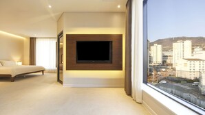 A modern hotel room with a large bed, a flat-screen TV mounted on the wall, and a city view through a large window. - Hermon Hotel Gangseo (Busan)