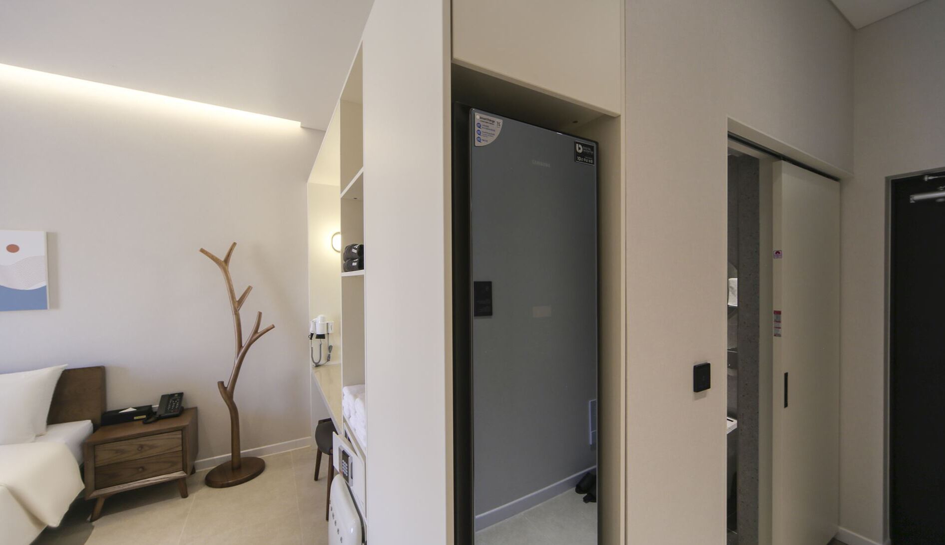 Una habitación de hotel con cama, mesita de noche, lámpara y perchero.