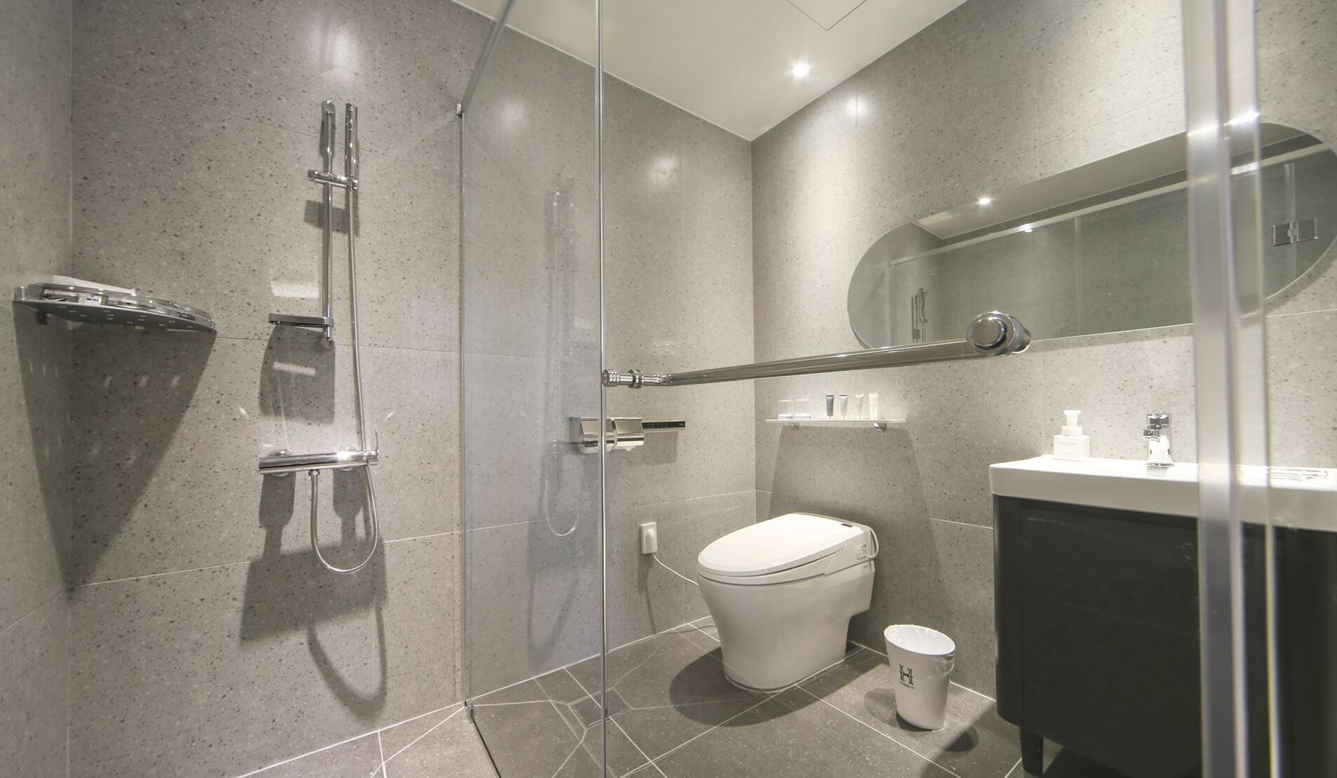 Un baño moderno con ducha envuelta en cristal, inodoro y lavamanos con espejo arriba.