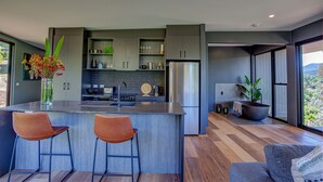 A modern kitchen with a central island, bar stools, and a large window offering a view of the outdoors. - The View Bright (Bright)
