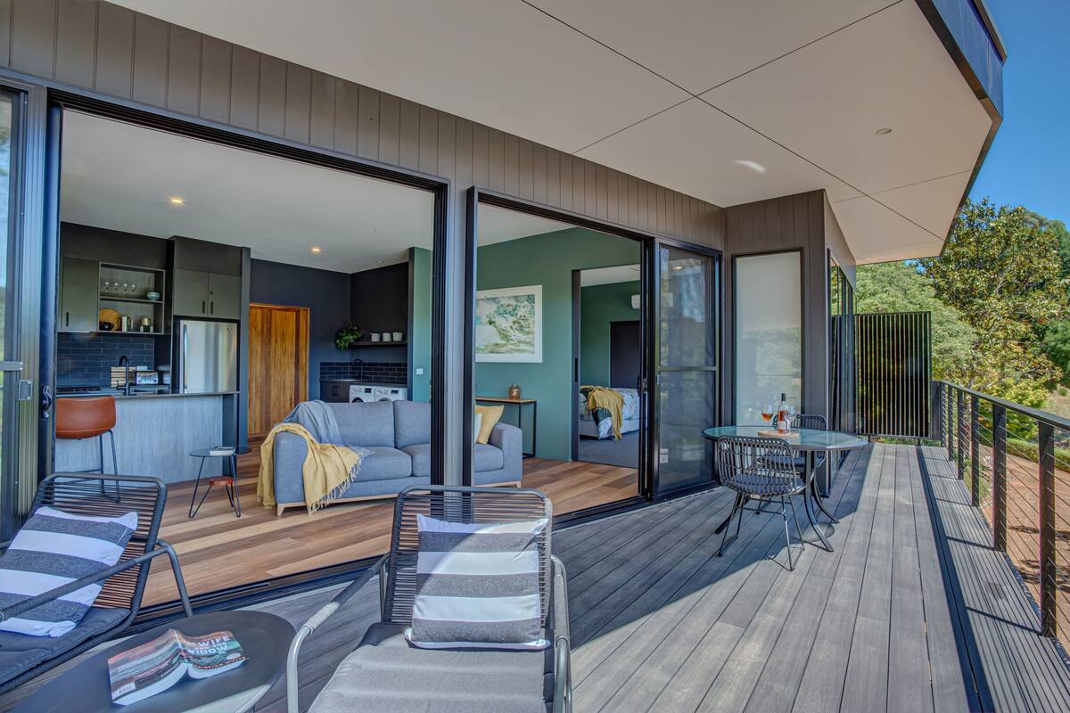 Une terrasse extérieure moderne dotée d’un espace repas, de chaises longues et d’une cuisine visible à travers des portes vitrées.
