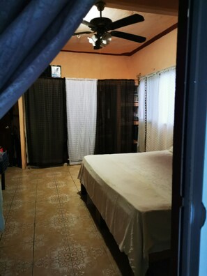 A bedroom with a bed, a ceiling fan, and curtains.