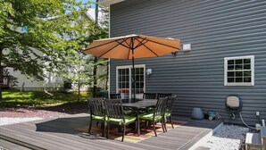A deck with a table and chairs, a patio umbrella, and a grill area. - Pocono’s Mountain winter getaway! (Tobyhanna)