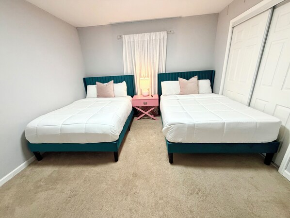 Un dormitorio con dos camas, una mesita de noche, una lámpara y una ventana con cortinas.