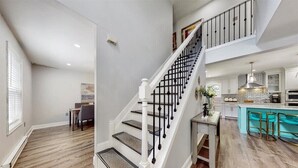 A spacious kitchen with a central island, a staircase with black railings, and a dining area with a table and chairs. - Pocono’s Mountain winter getaway! (Tobyhanna)