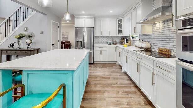 A modern kitchen with white cabinetry, a large island, stainless steel appliances, and a wooden floor. - Pocono’s Mountain winter getaway! (Tobyhanna)