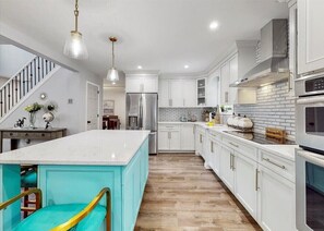 Una cocina moderna con armarios blancos, una isla grande, electrodomésticos de acero inoxidable y piso de madera.