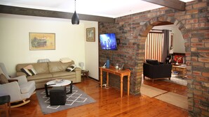 Ein Wohnzimmer mit Holzboden, einer Couch, einem Couchtisch und einem an einer Ziegelwand befestigten Fernseher.