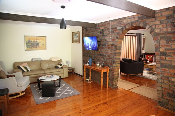 A living room with a wooden floor, a sofa, a coffee table, and a TV mounted on a brick wall.