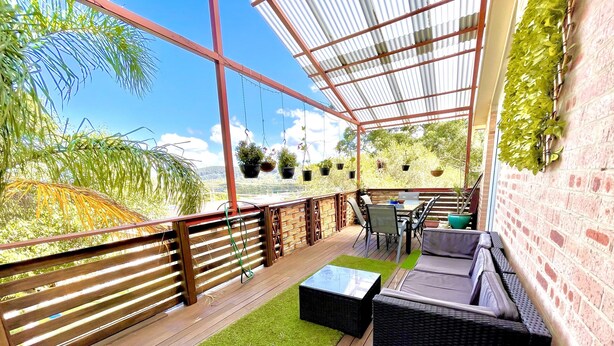 Eine überdachte Terrasse mit Holzdeck, Gartenmöbeln und hängenden Pflanzgefäßen.