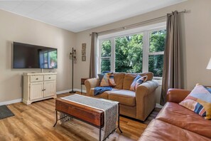 A living room with a sofa, a coffee table, a TV, and a window with curtains.