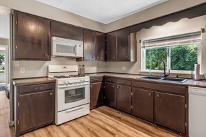 A kitchen with dark wooden cabinets, a white stove, and a window with a view of greenery.