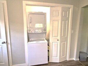 A laundry room with a washer and dryer, a door, and a trash can.