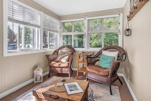 A sunroom with wicker chairs, a small table, and a view of the outdoors. - Steps from 1st St Beach, Large Yard, Firepit (South Haven)