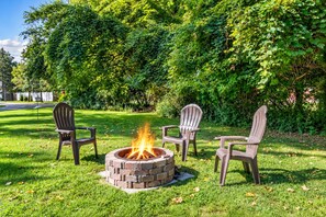 Un foyer extérieur entouré de trois chaises Adirondack, situé dans un espace herbeux avec des arbres en arrière-plan.