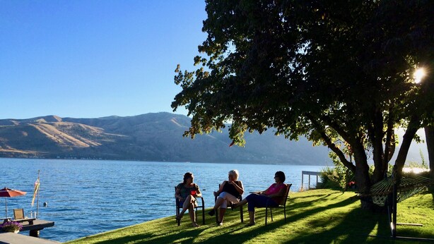 A lakeside setting with a grassy area, a hammock, and a table with chairs.