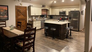 A modern kitchen with white cabinets, a central island with stools, a stainless steel refrigerator, and a ceiling fan.
