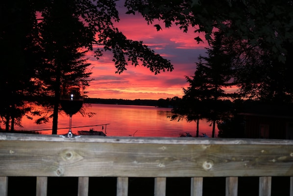 A wooden deck overlooking a lake at sunset with a clear view of the water and distant shoreline.