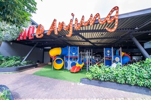 Un espace de jeux extérieur avec des toboggans et des structures d’escalade, entouré de verdure et doté d’un espace de repos abrité.