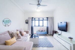 A modern living room with a sofa, coffee table, and TV. There is a window with curtains and a ceiling fan.