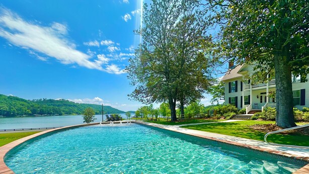 A swimming pool with a clear view of a lake and a house in the background.