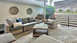 An outdoor patio area with wicker furniture, a glass-top table, and a decorative light fixture.