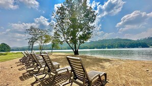 A row of sun loungers on a sandy beach with a lake and trees in the background.