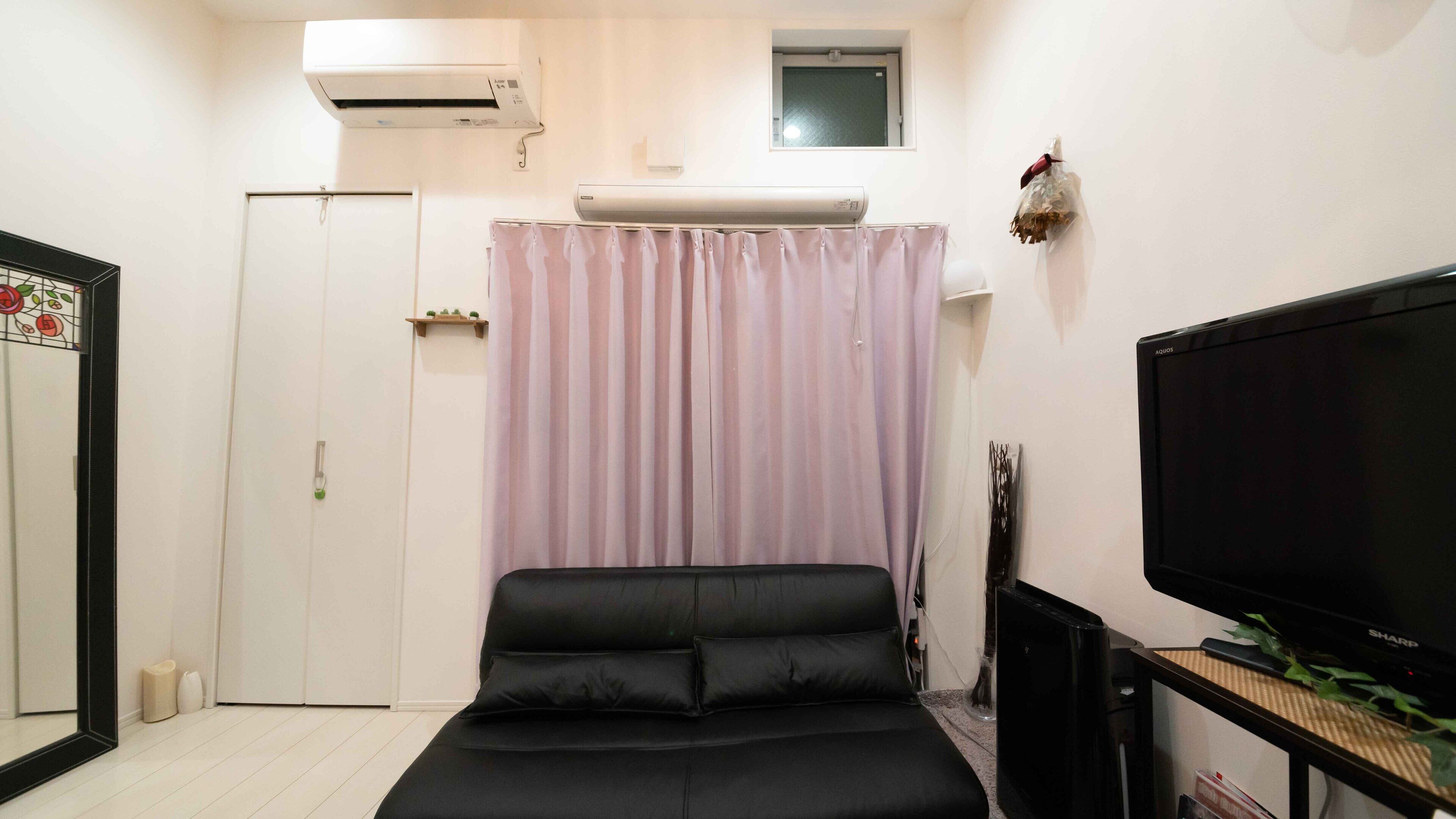 Une petite chambre à coucher, bien rangée, avec un lit, un téléviseur et un appareil de climatisation.