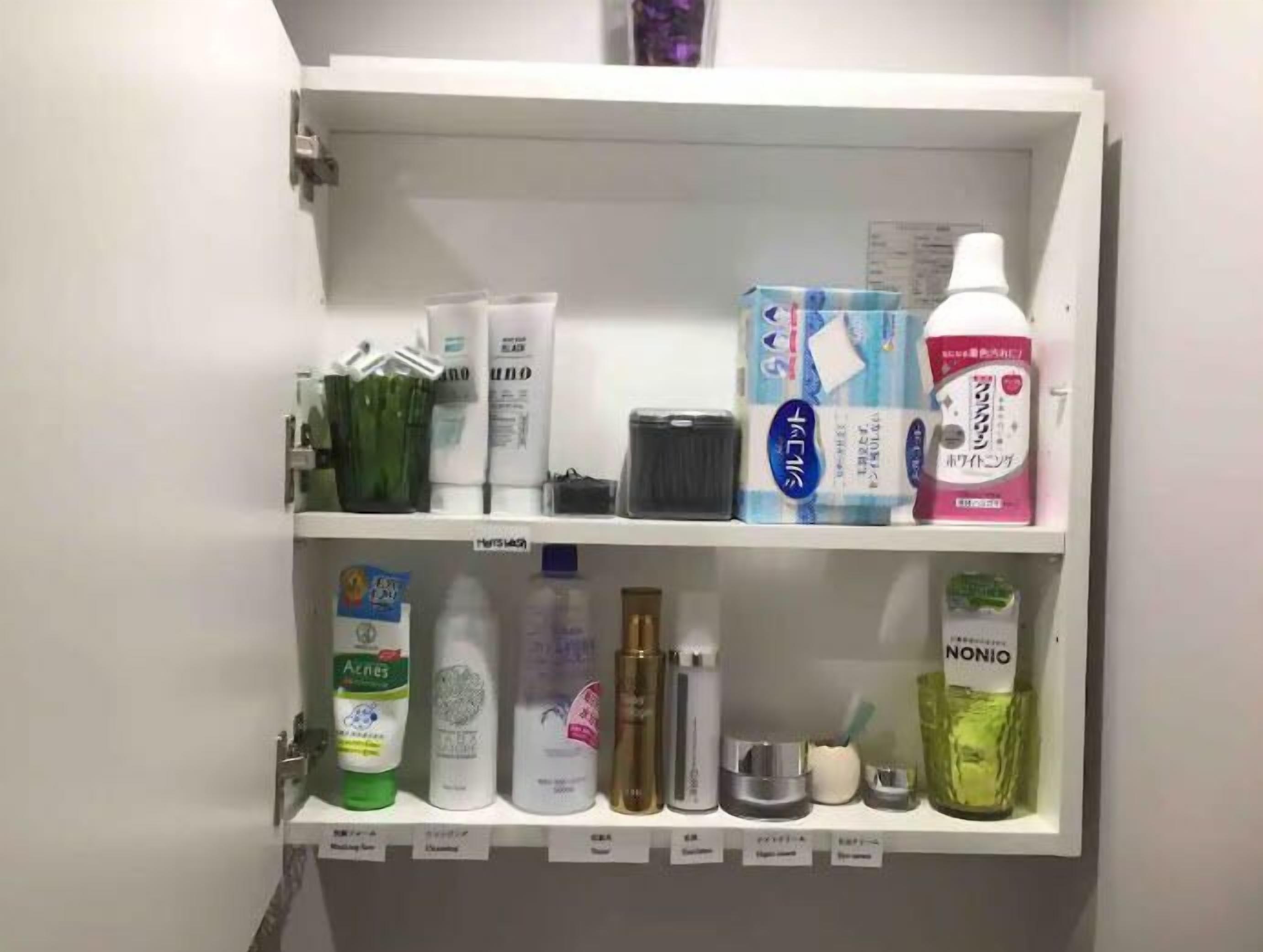 A bathroom cabinet with various toiletries including a green bottle labeled 'Aznes', a white bottle labeled 'NONIO', and a pink bottle labeled 'NANON'.