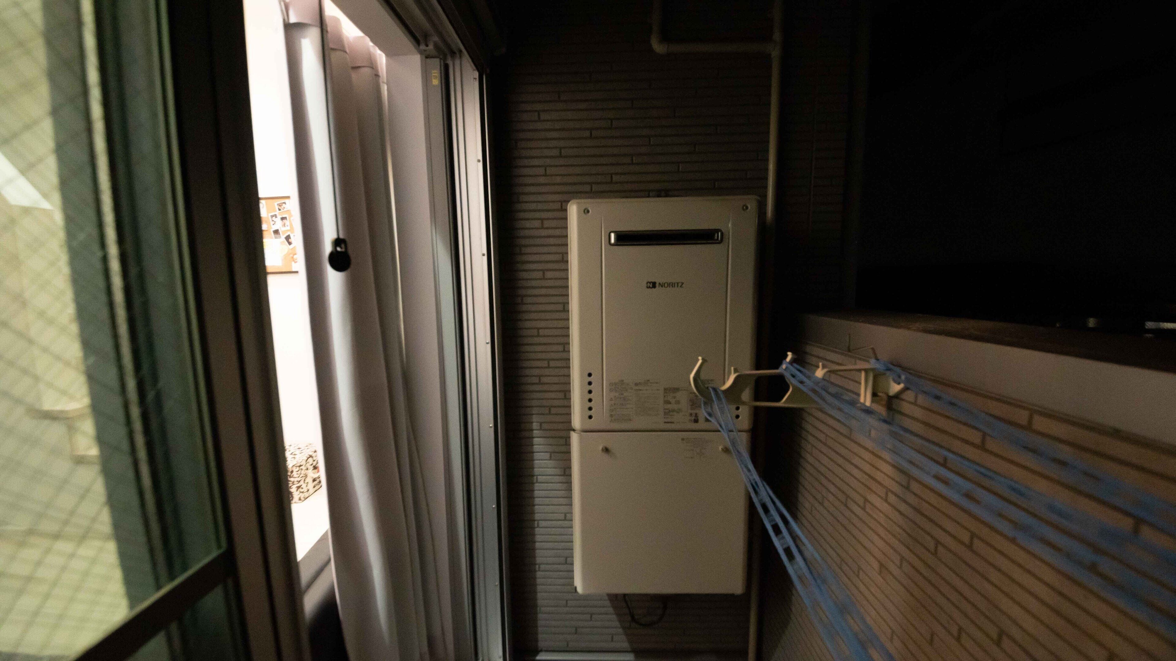Un cuarto de servicio con un panel eléctrico Noritz, una puerta y una ventana con persianas.