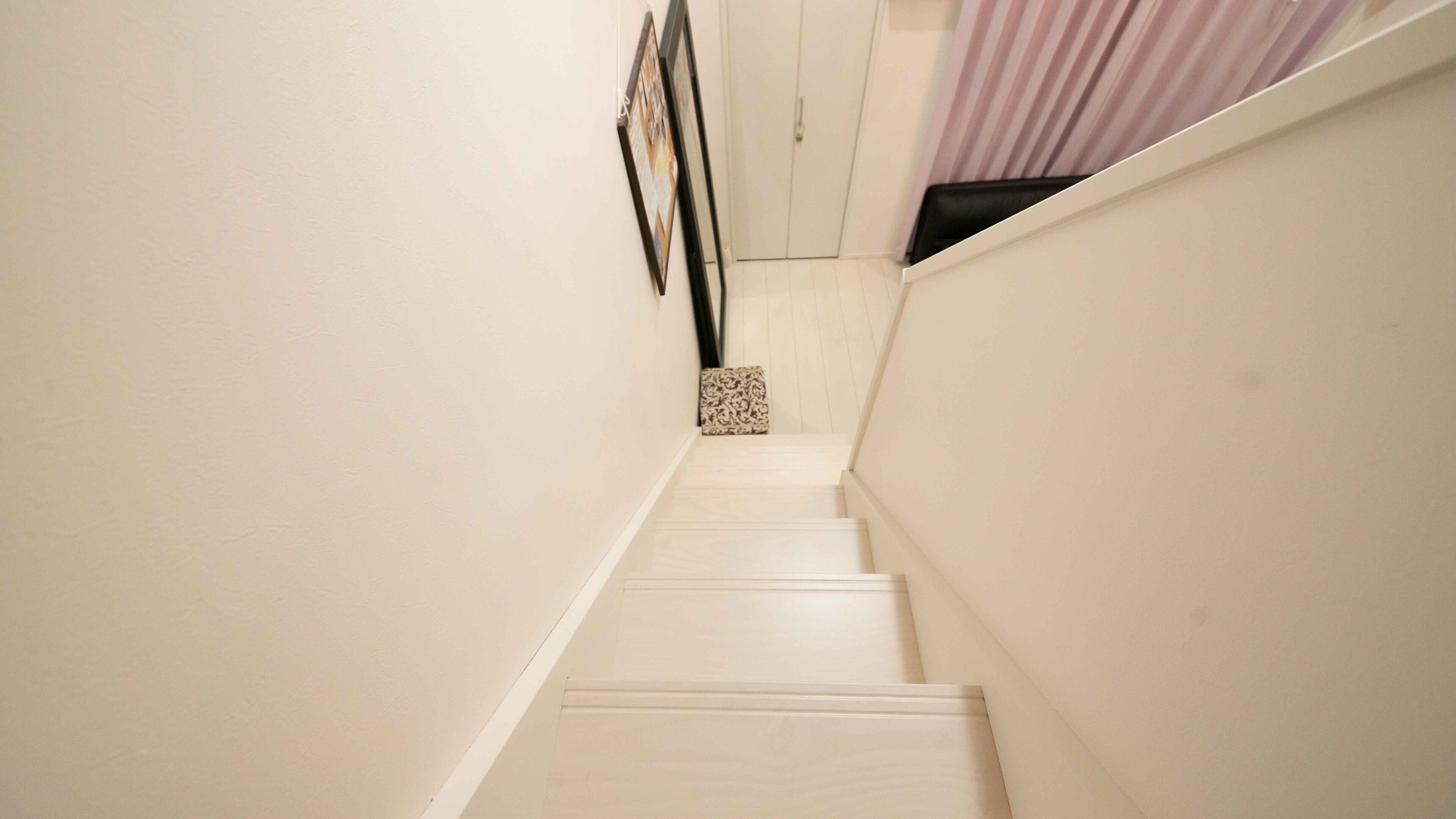 A narrow staircase with white walls and a patterned cushion at the bottom landing.