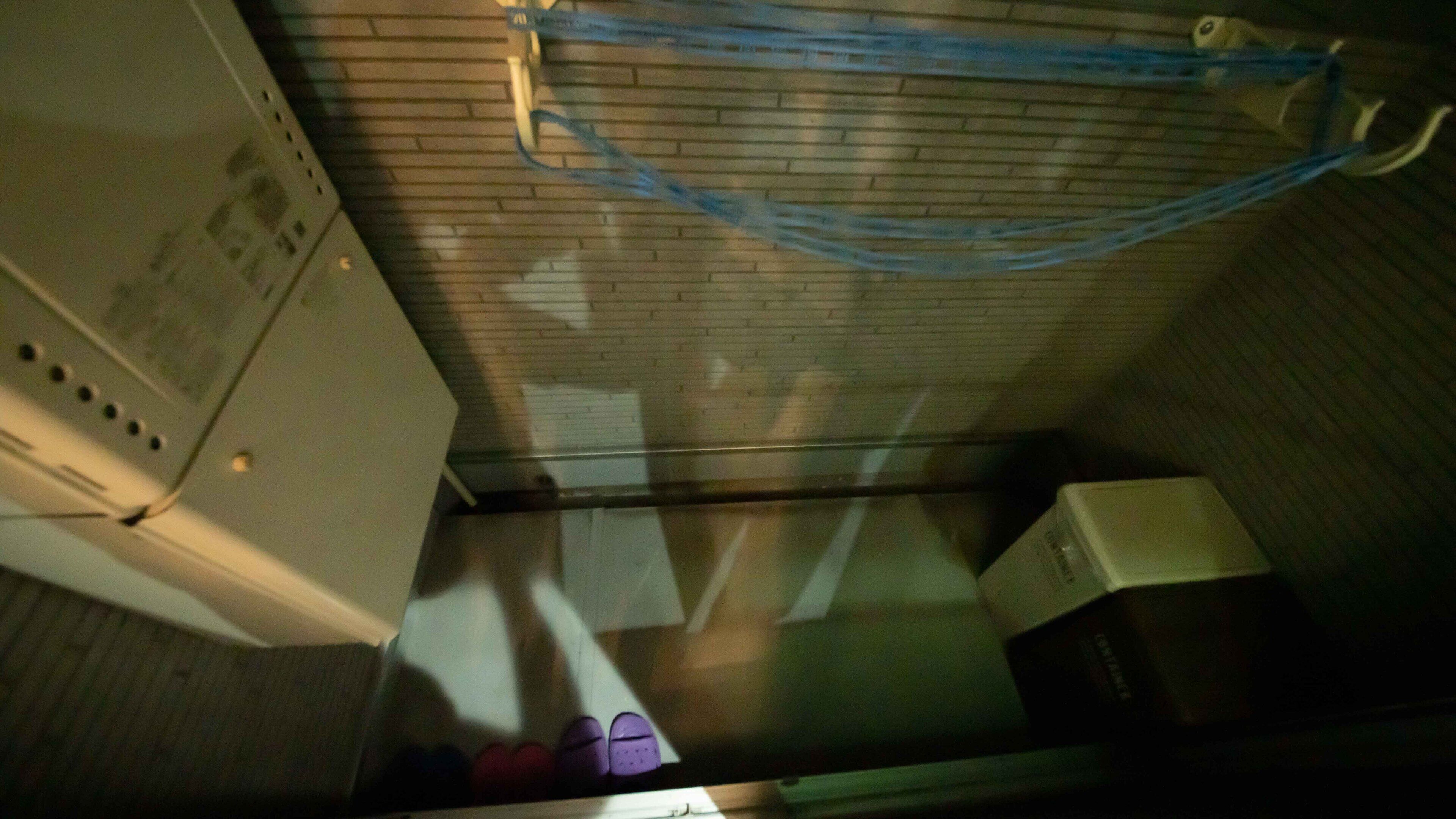A narrow corridor with a ceiling-mounted blue safety rail, a white appliance on the left, and a box on the right.