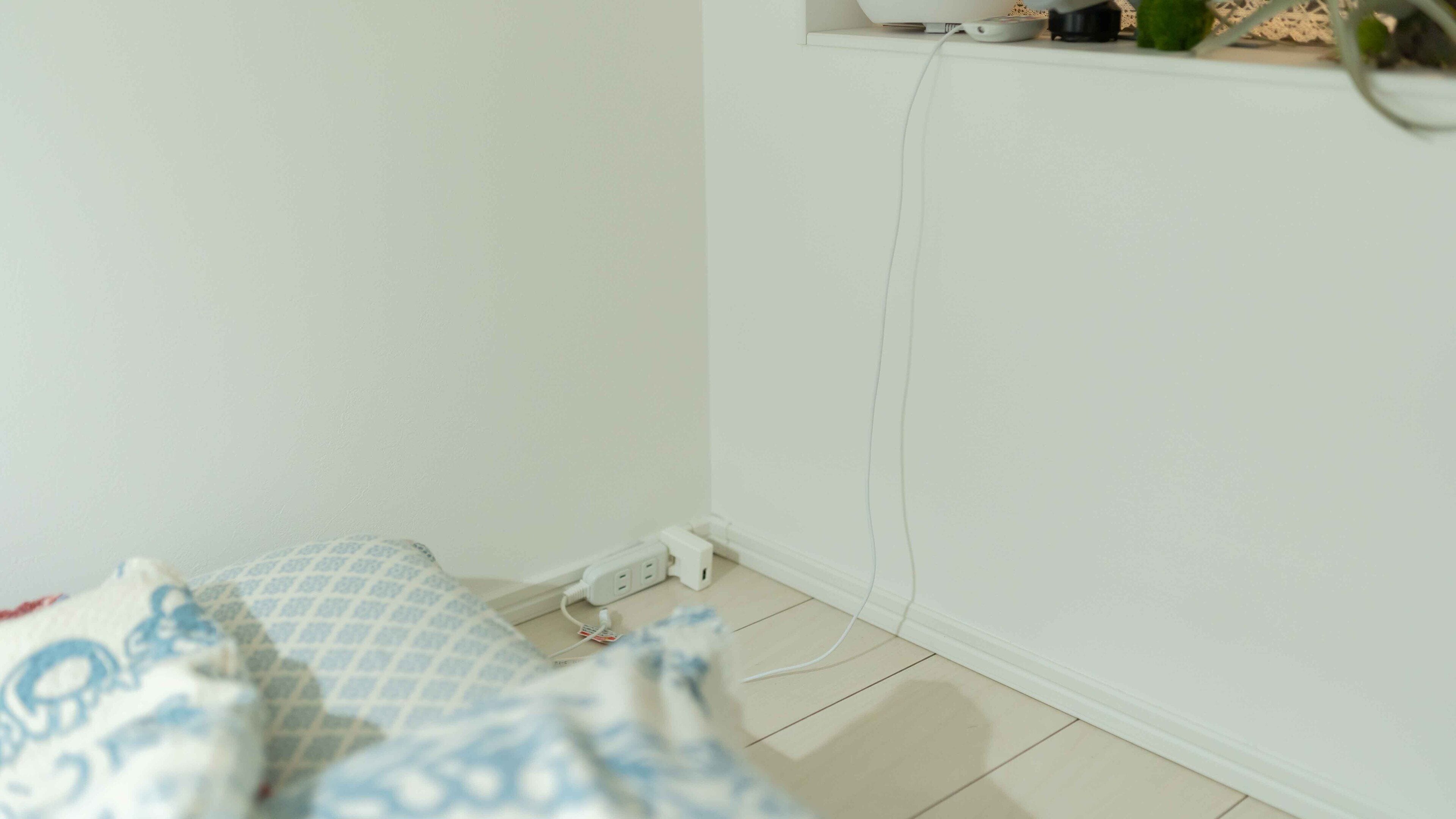 A bedroom with a bed, a white wall, and a power outlet.