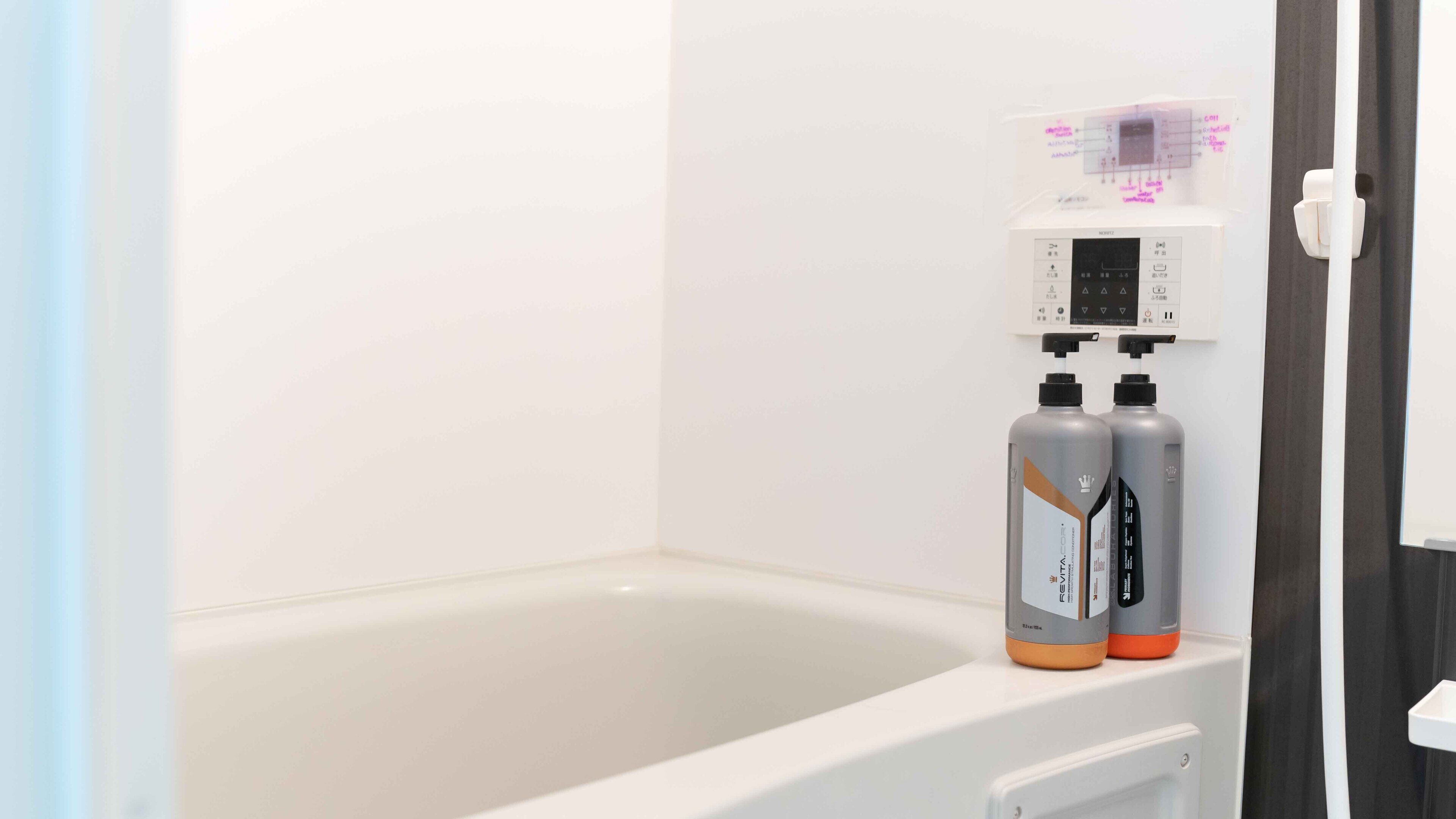 A bathroom with a bathtub, a control panel above it, and two bottles of shampoo.