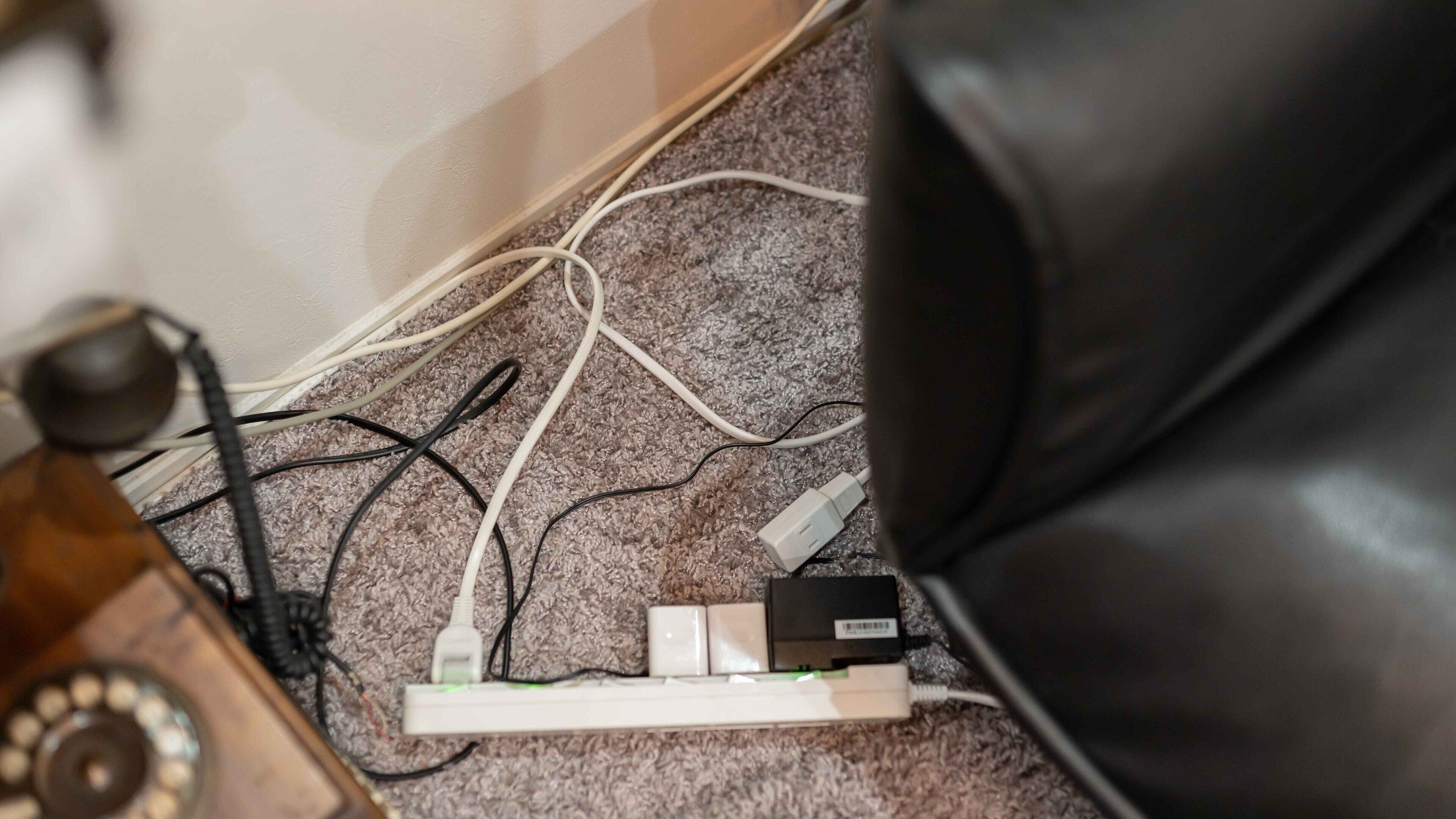 A cluttered room with various cables and electronic devices on a carpeted floor.