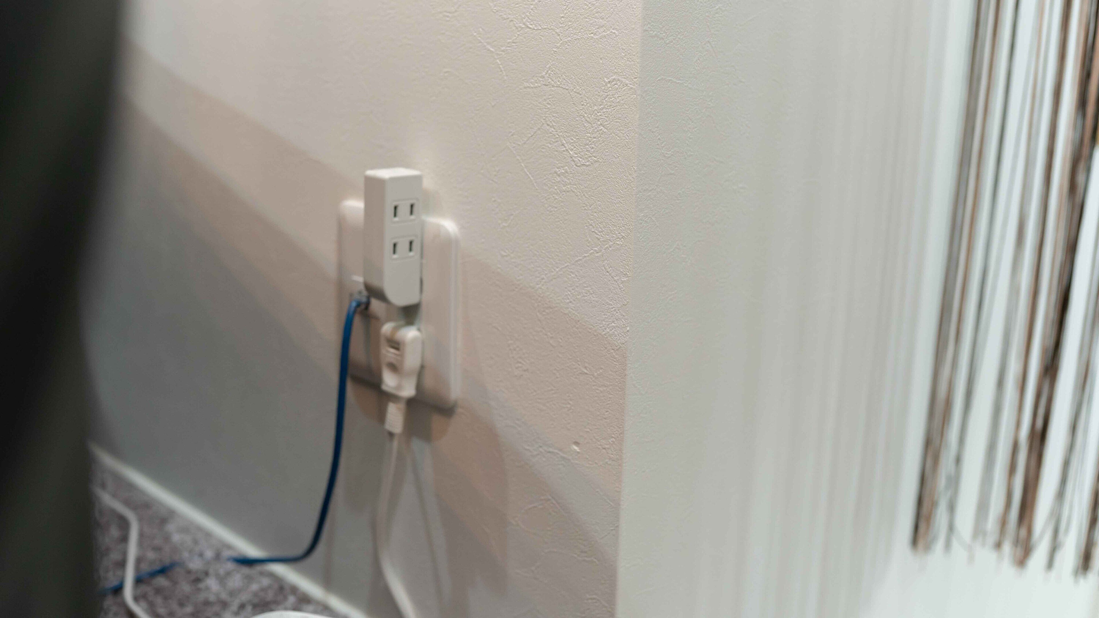 A white electrical outlet with a blue cable plugged in, located on a wall with a textured finish.