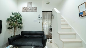 Una sala de estar con un sofá de cuero negro, una planta en maceta y una escalera.