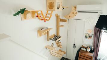 A room with a wooden cat tree, a calendar, a small desk with a chair, and a window with curtains.