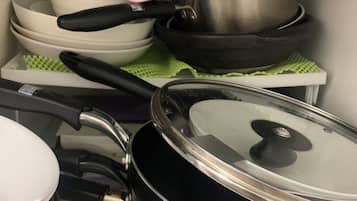 Een keuken met diverse kookgerei, waaronder pannen, braadpannen en een koekenpan.