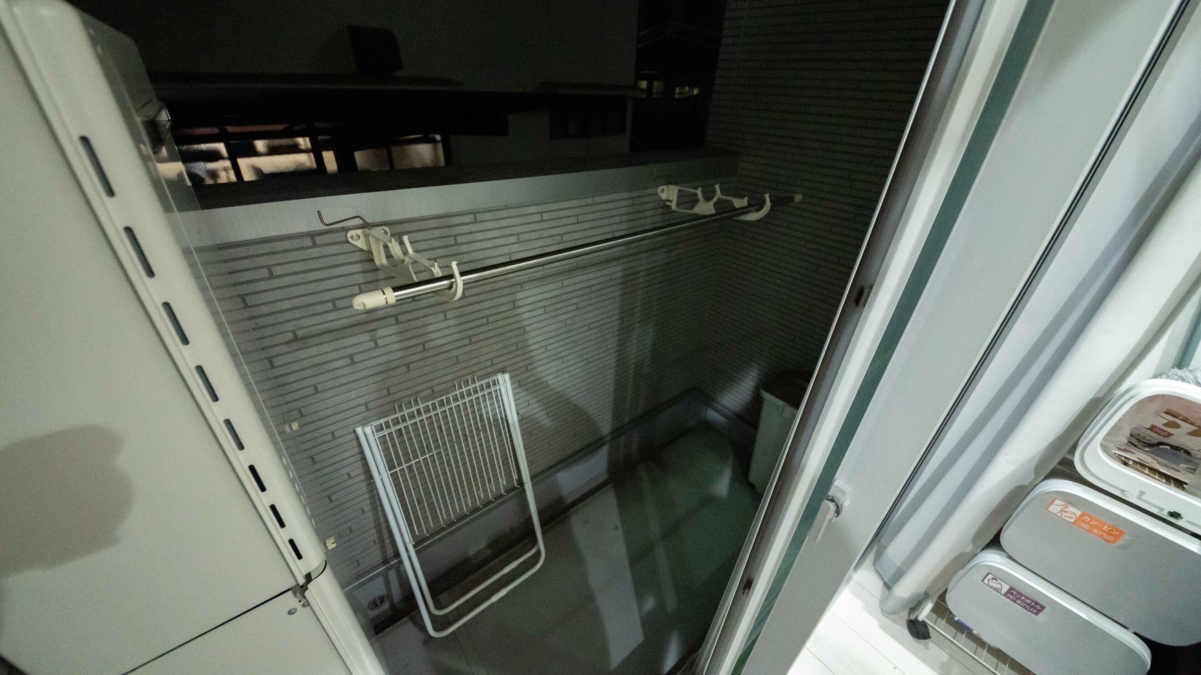 Ein Hotelzimmer mit gefliesten Wänden, einem Metallregal und einem kleinen Fenster.