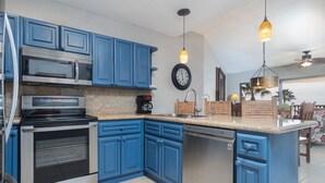 Una cocina con armarios azules, electrodomésticos de acero inoxidable, encimera de granito e iluminación colgante.